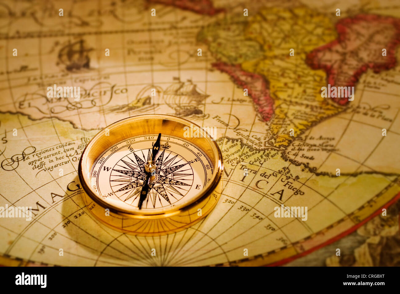 An antique gold compass set upon a sixteenth century map of the world Stock Photo
