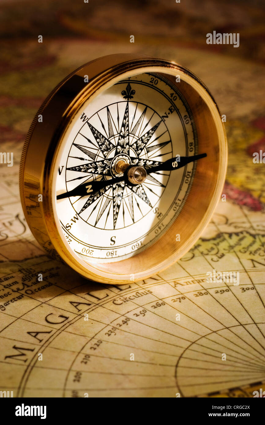 An antique gold compass set upon a sixteenth century map of the world Stock Photo