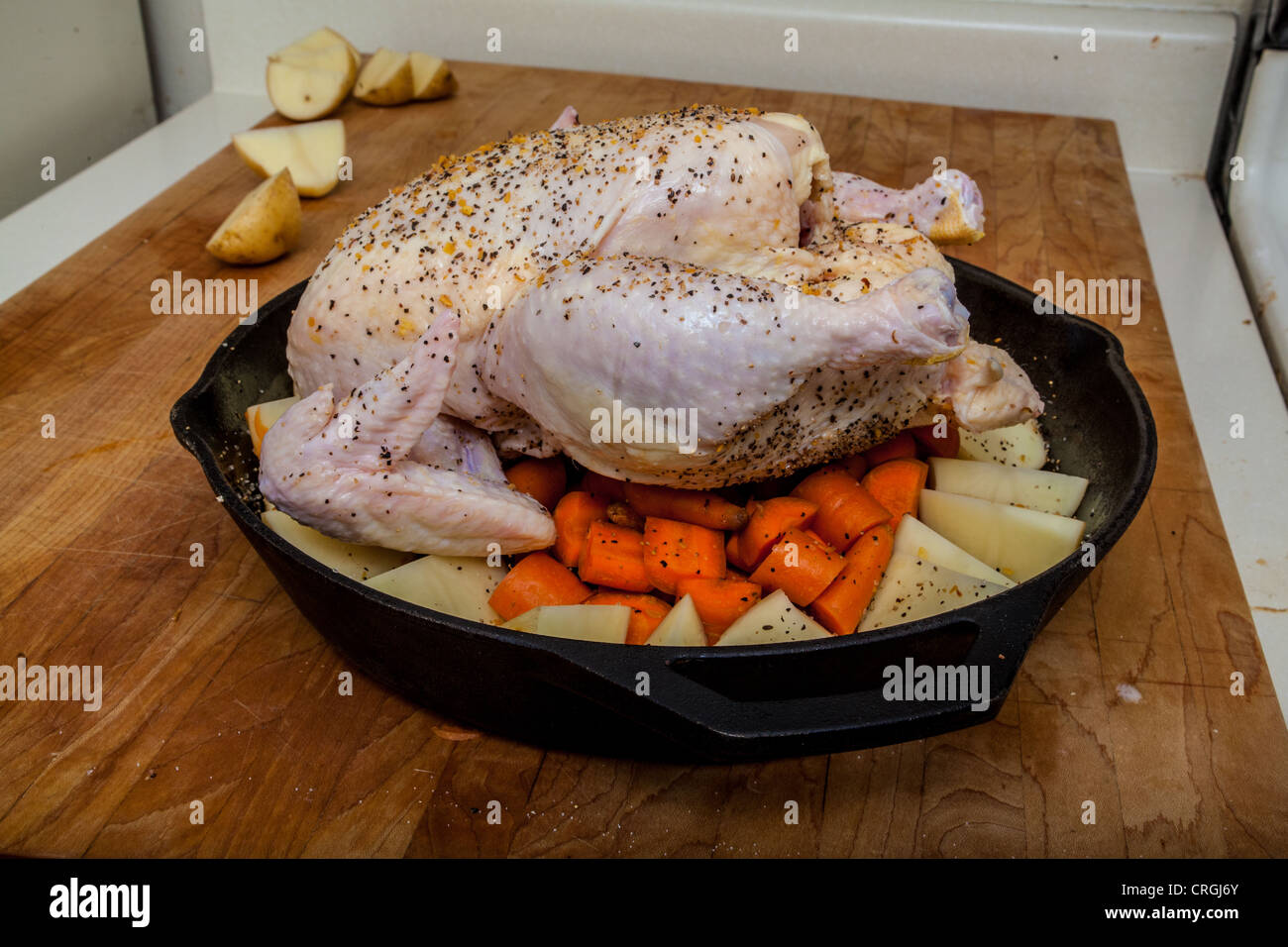 A raw chicken prepared for roasting with potatoes and carrots in a cast