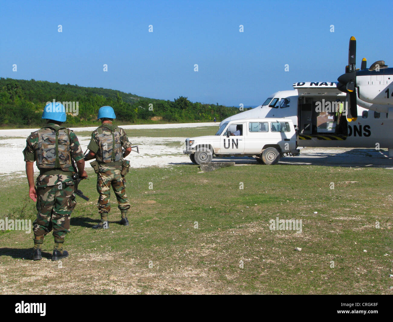 Soldiers of the 'United Nations Stabilisation Mission in Haiti' secure UN aircraft with machine gun and assault rifle next to unpaved runway, Haiti, Grande Anse, Jeremie Stock Photo