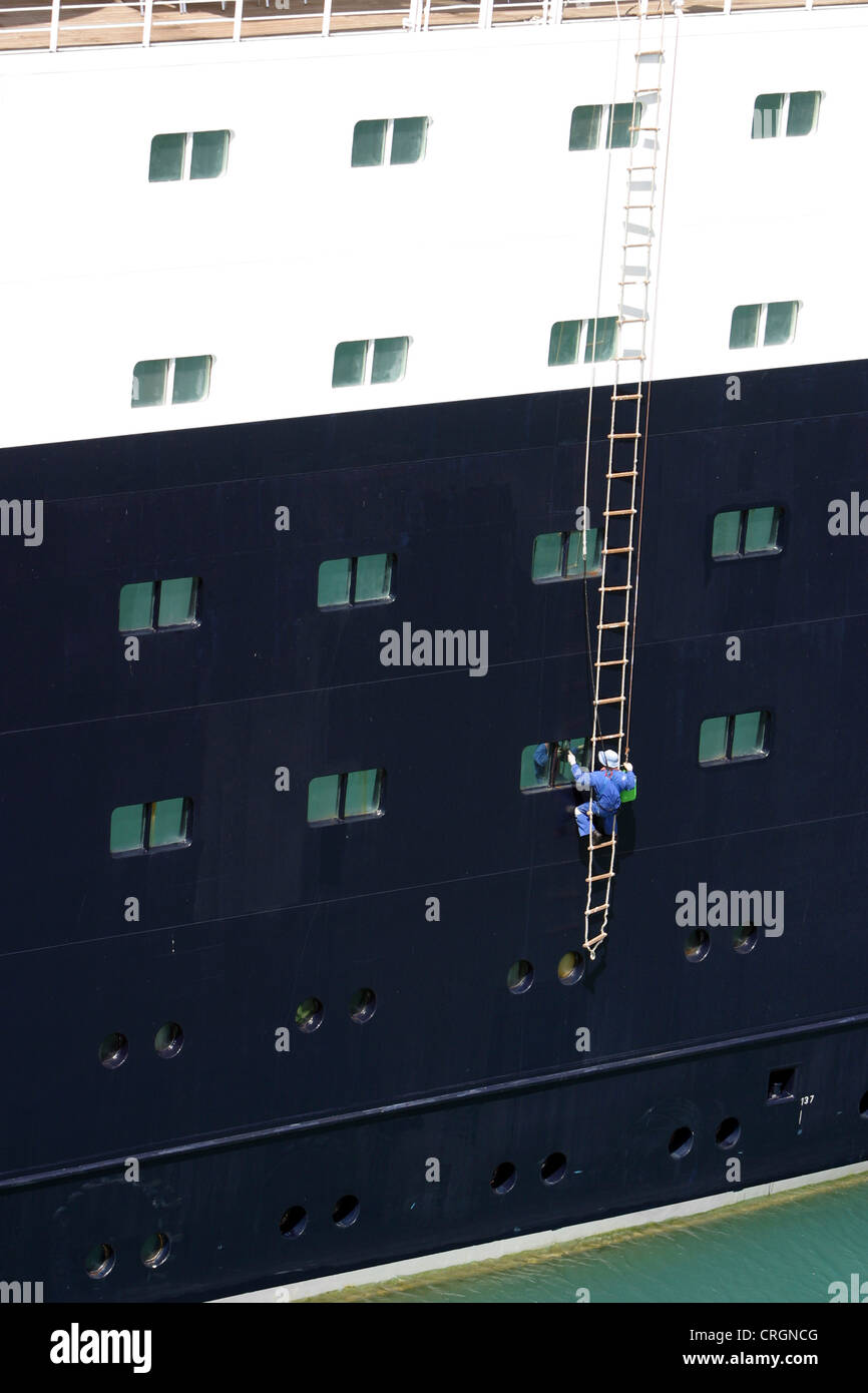 man on a rope ladder painting a ship Stock Photo