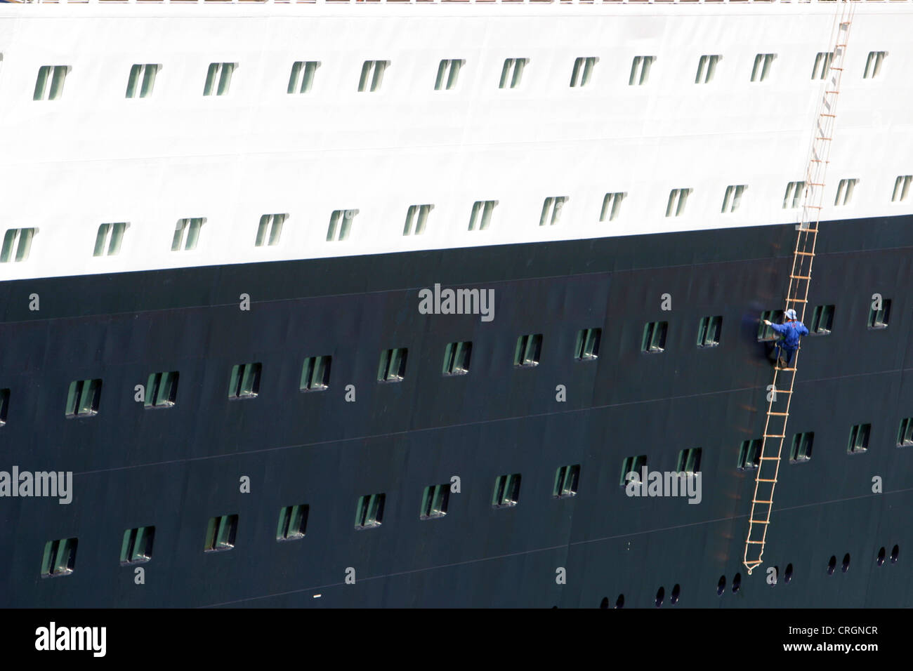 man on a rope ladder cleaning windows of a ship Stock Photo