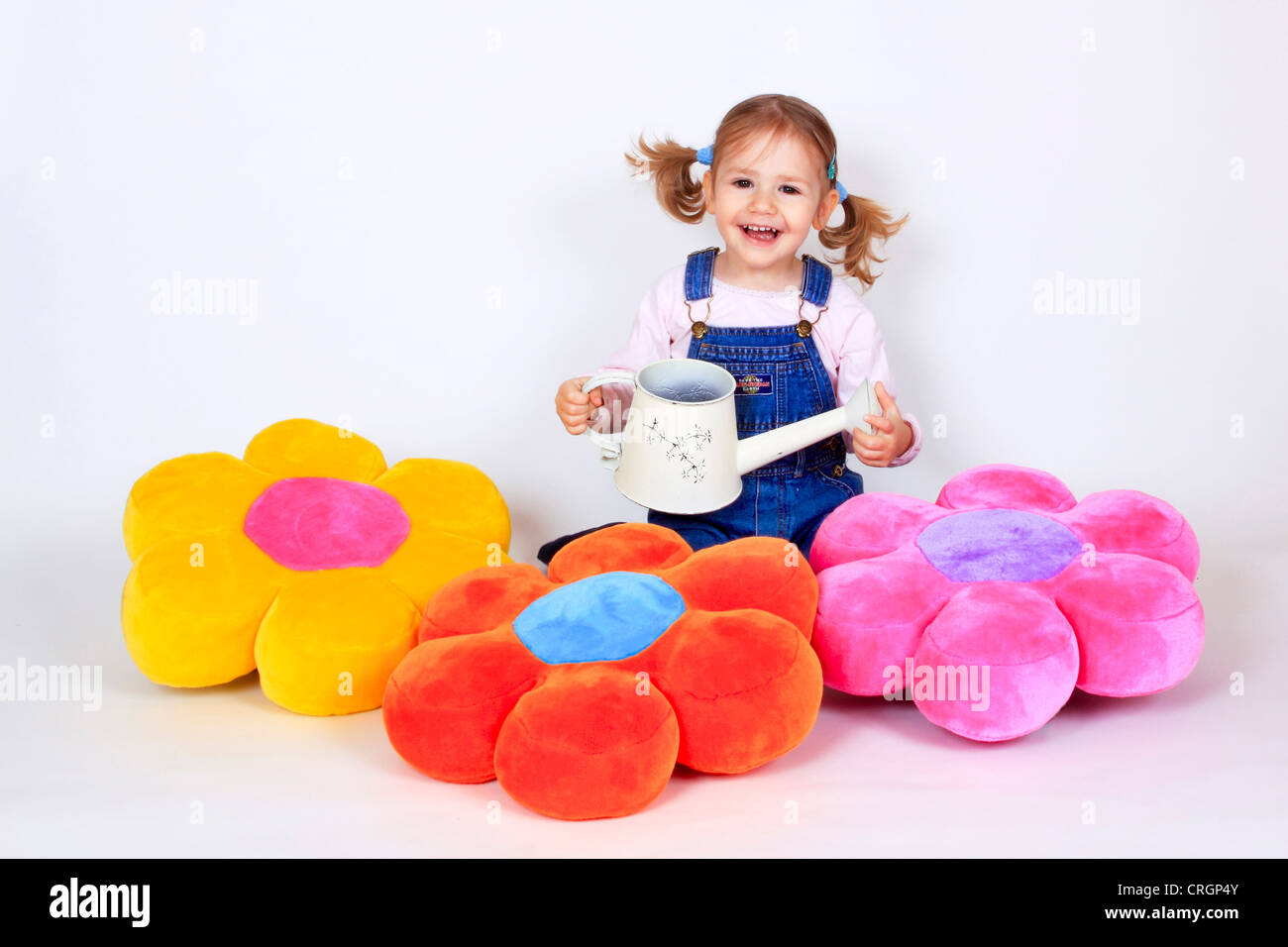 little girl waters flower pillows with watering can Stock Photo