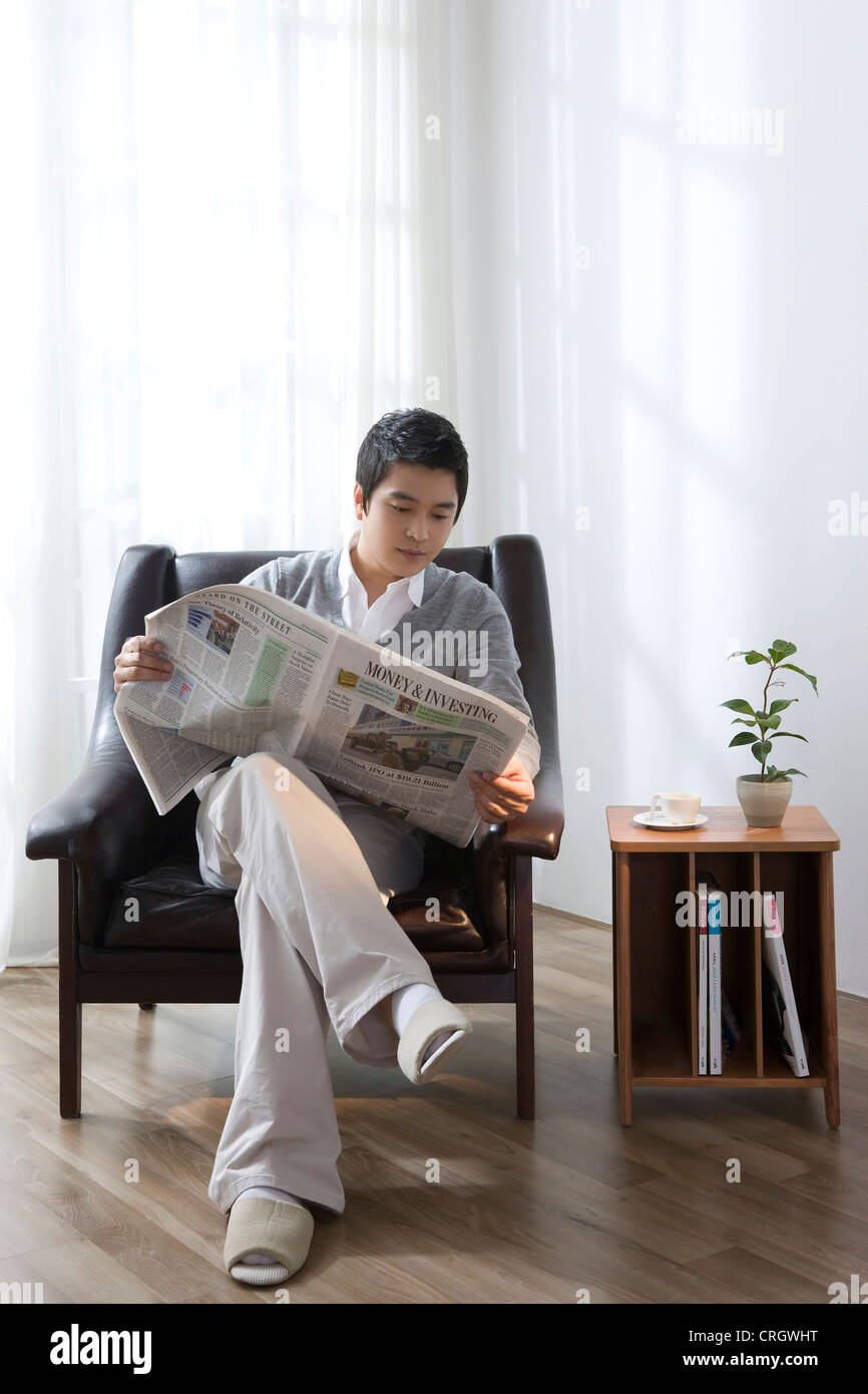 Young man reading a newspaper in the livingroom Stock Photo - Alamy