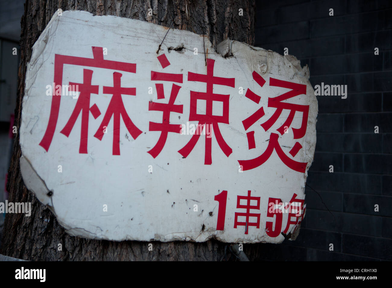 Ruined placard with Chinese text displayed on tree trunk, Beijing, China Stock Photo
