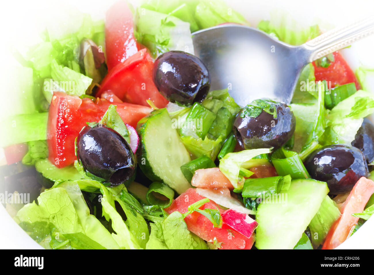 Closeup photo of fresh side dish with green salad, tomatoes, olives, cucumbers and a metal spoon Stock Photo