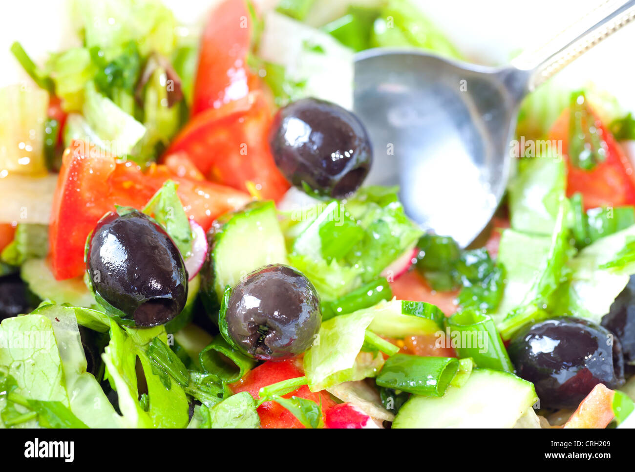 Closeup photo of fresh side dish with salad, tomatoes, olives, cucumbers and a metal spoon Stock Photo