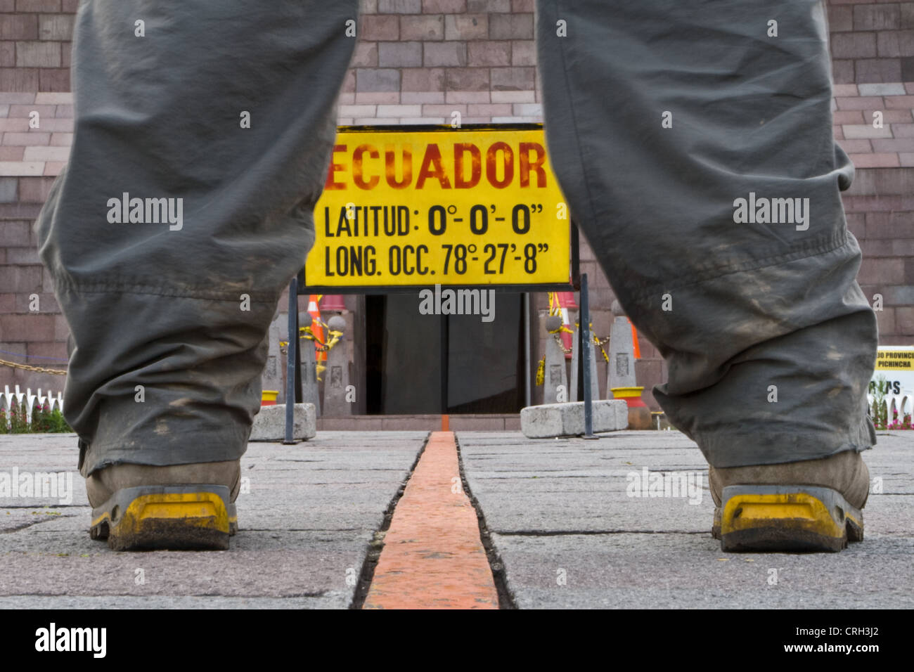 A man standing over the equator line, one foot in the northern and southern hemisphere near Quito, Ecuador. Stock Photo