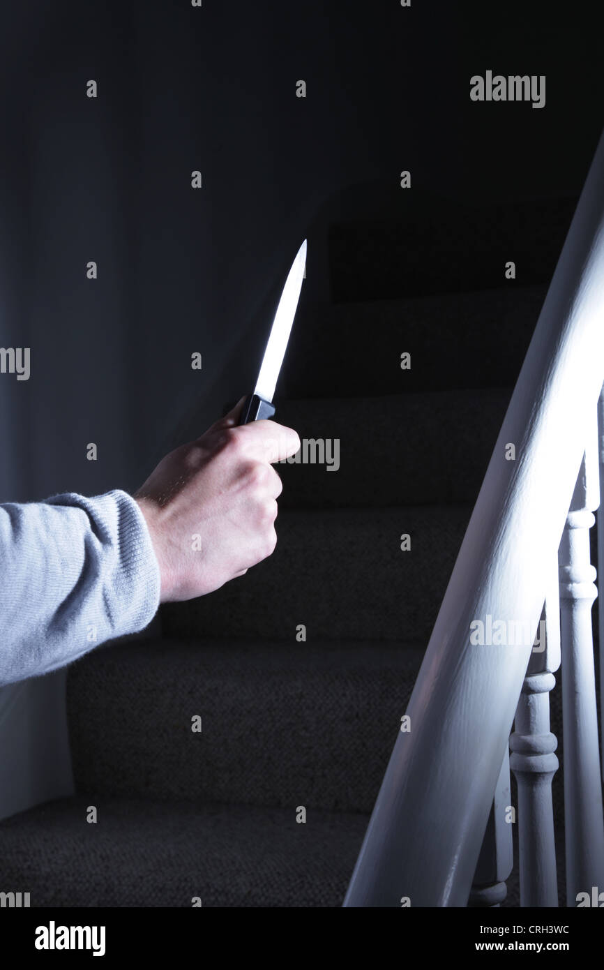 Male hand holding a knife walking upstairs. Stock Photo