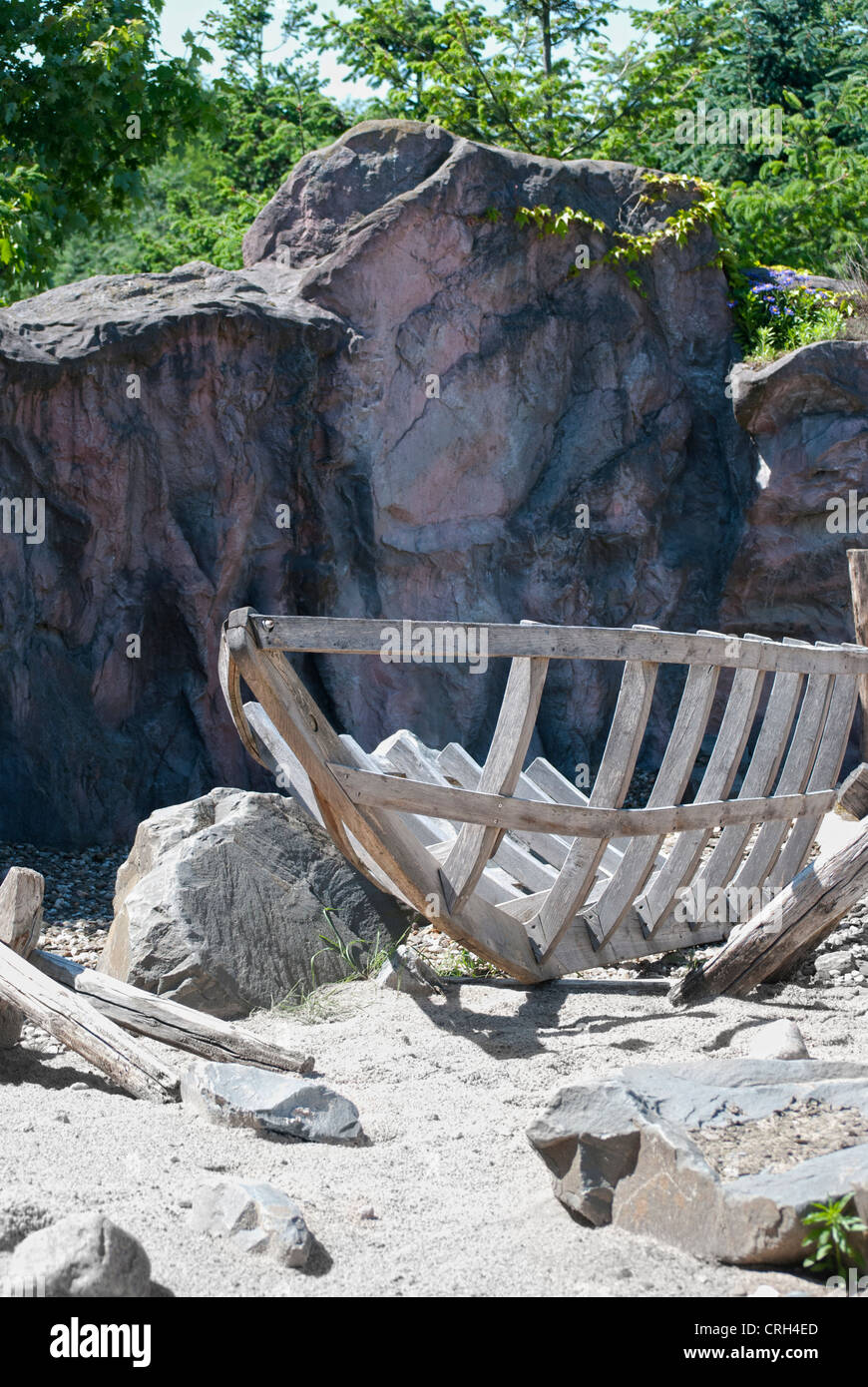 Wooden boat construction on dark stones and green trees background Stock Photo