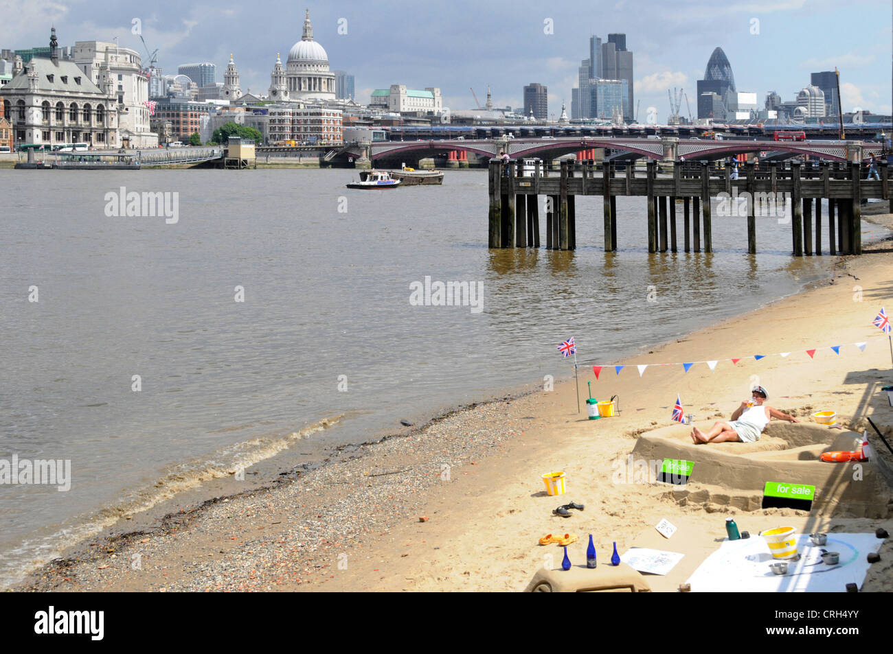 Low tide sandy beach beside River Thames man creating sand sculptures with City of London skyline beyond (phone numbers deleted) Stock Photo