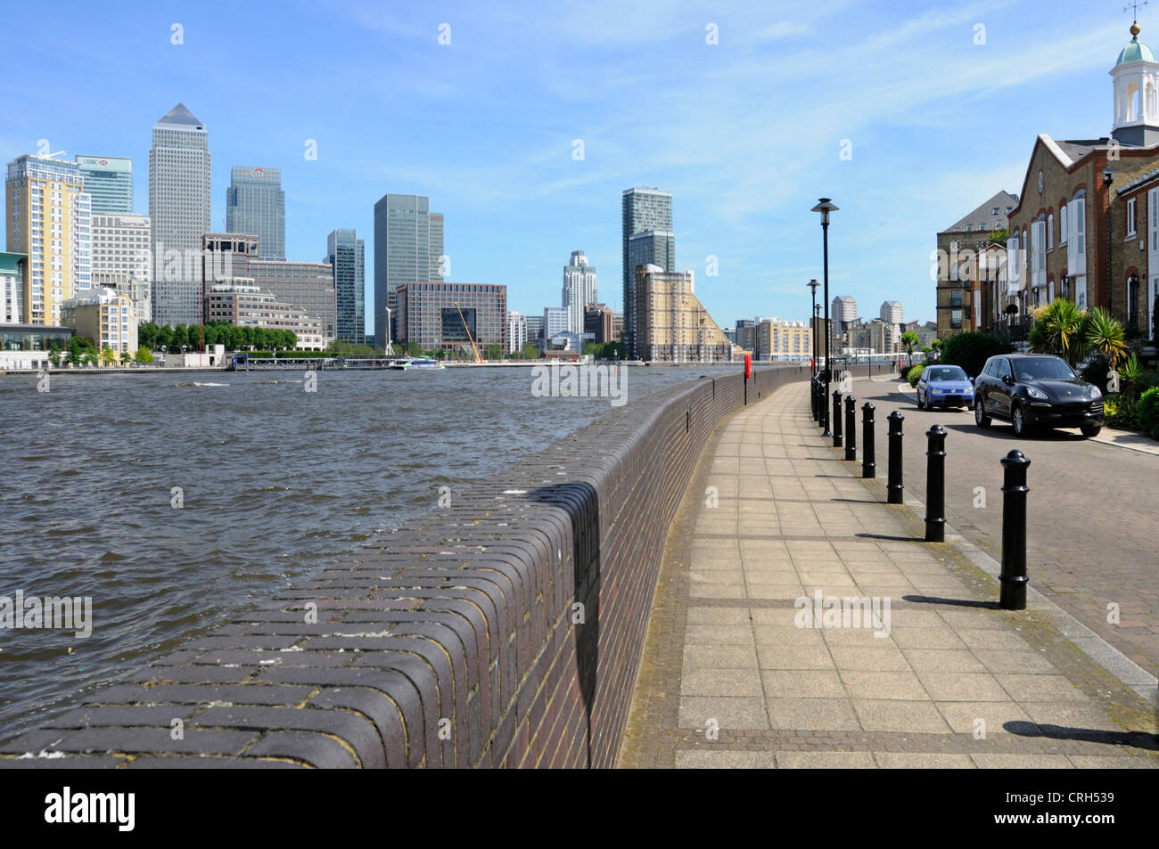 View across River Thames at high tide towards London Docklands Canary Wharf skyline includes brick flood defence wall Stock Photo