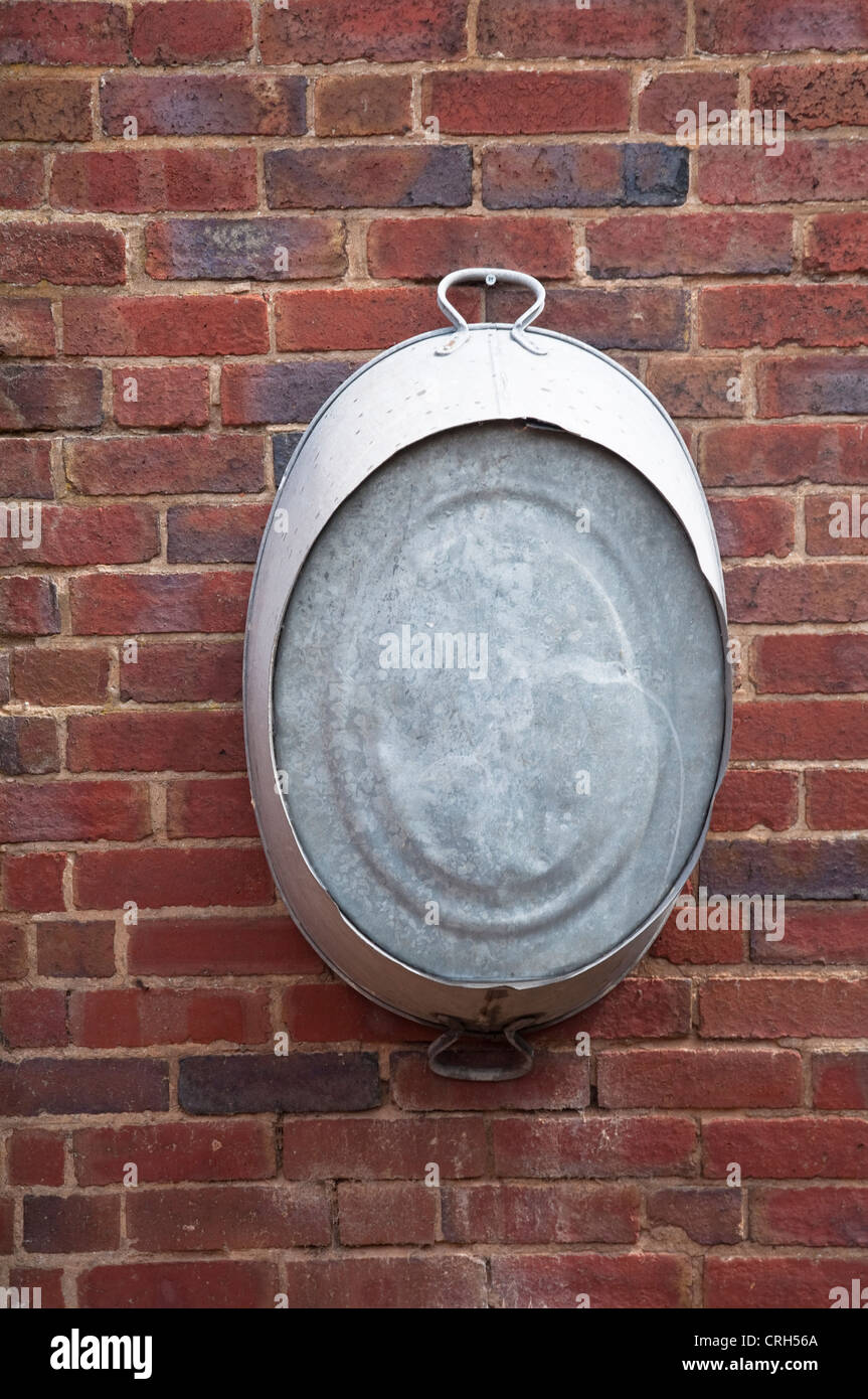 A tin bath or old galvanised metal tub, hanging on an outside brick wall. UK Stock Photo