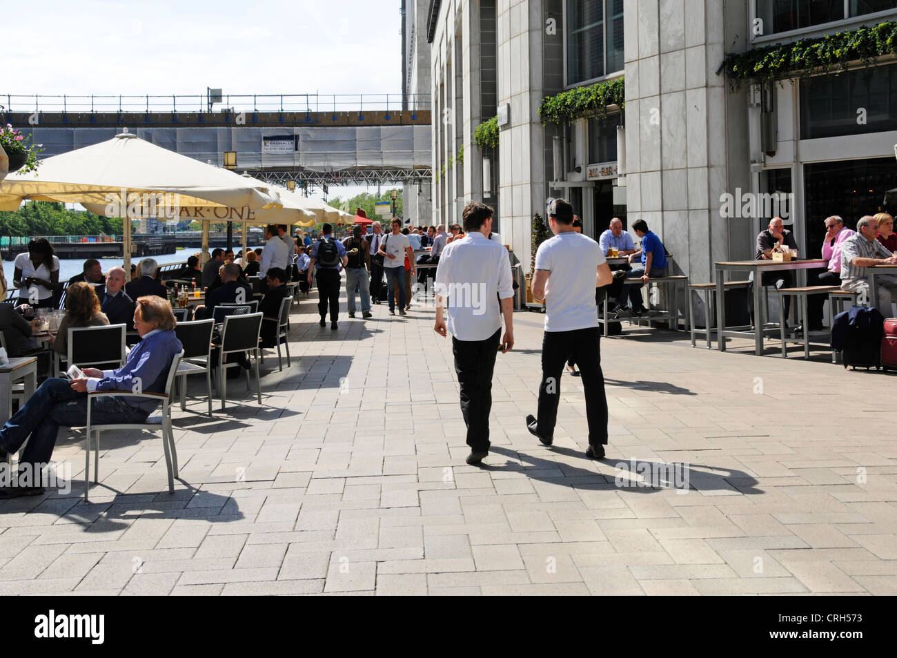 Summer sunshine eating & drinking outdoors cafe bar tables under shade from parasols Canary Wharf Isle of Dogs Tower Hamlets, East London England UK Stock Photo