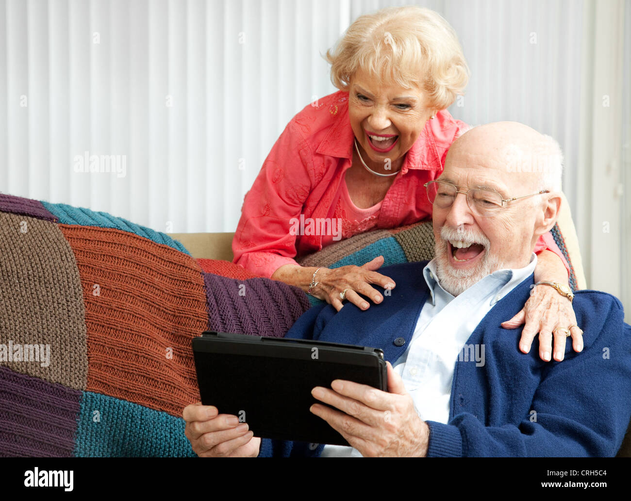 Senior couple laughing while using their tablet pc to video chat with their grandkids.  Stock Photo