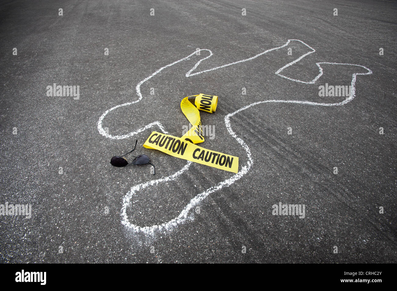 Caution tape and broken sun glasses rest near a chalk line from an auto accident. Stock Photo