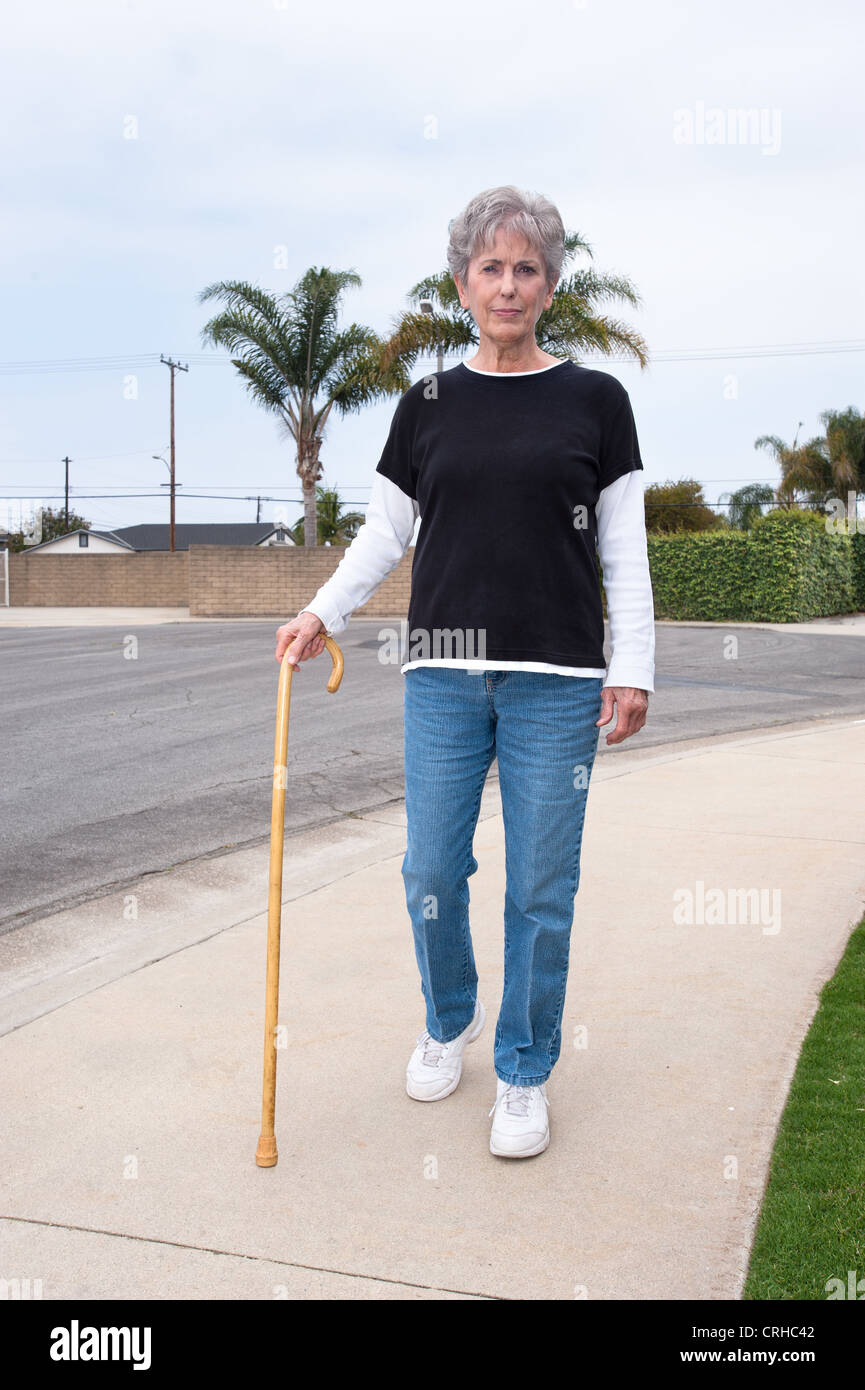 A woman uses a wooden cane to assist her while walking down a sidewalk. Stock Photo