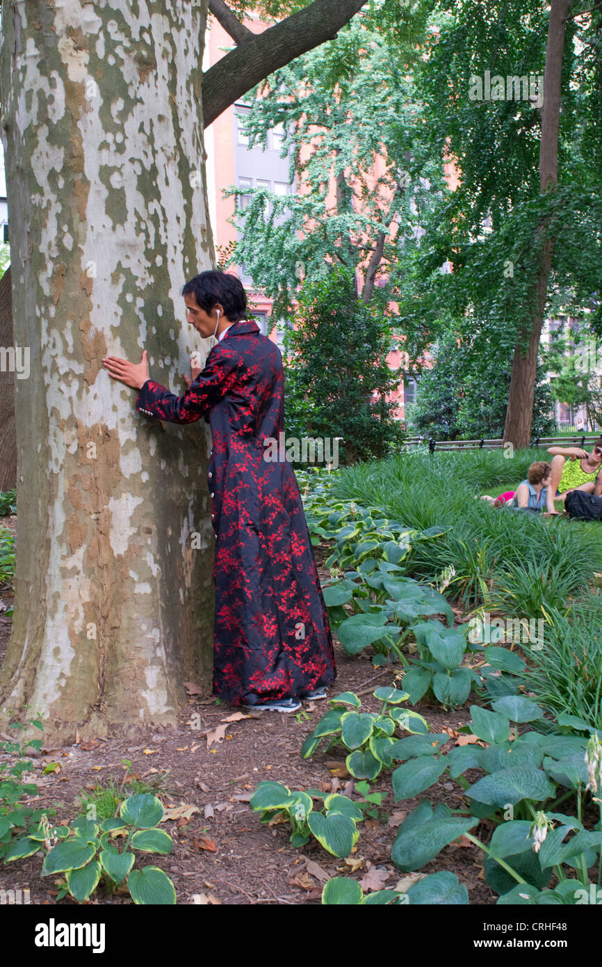 A tree hugger in an exotic colorful robe hugs a tree in Washington Square Park, Greenwich Village, New York Stock Photo