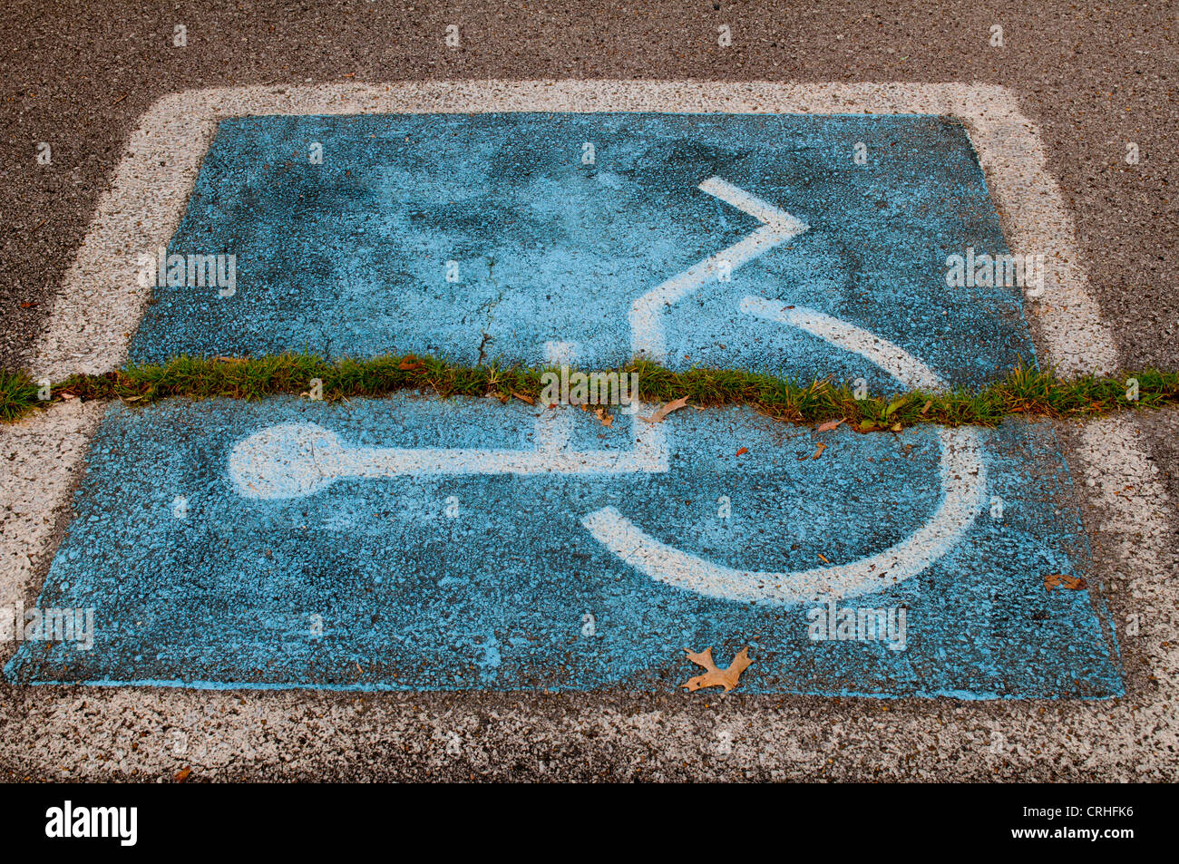 Handicap wheel chair symbol painted on parking space with grass growing through it Stock Photo