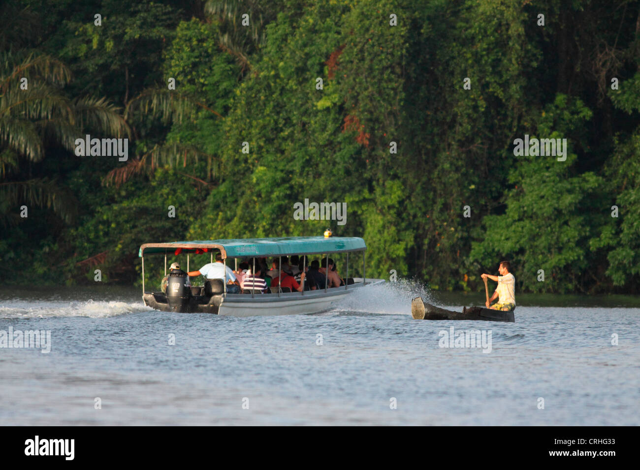 Tourist boat passes villager in canoe on natural rainforest canal. Tortuguero National Park. Costa Rica. October 2011. Stock Photo