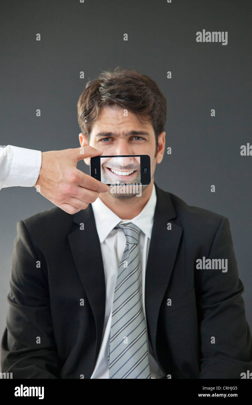 Man with mouth concealed behind smartphone displaying image of his own smile Stock Photo