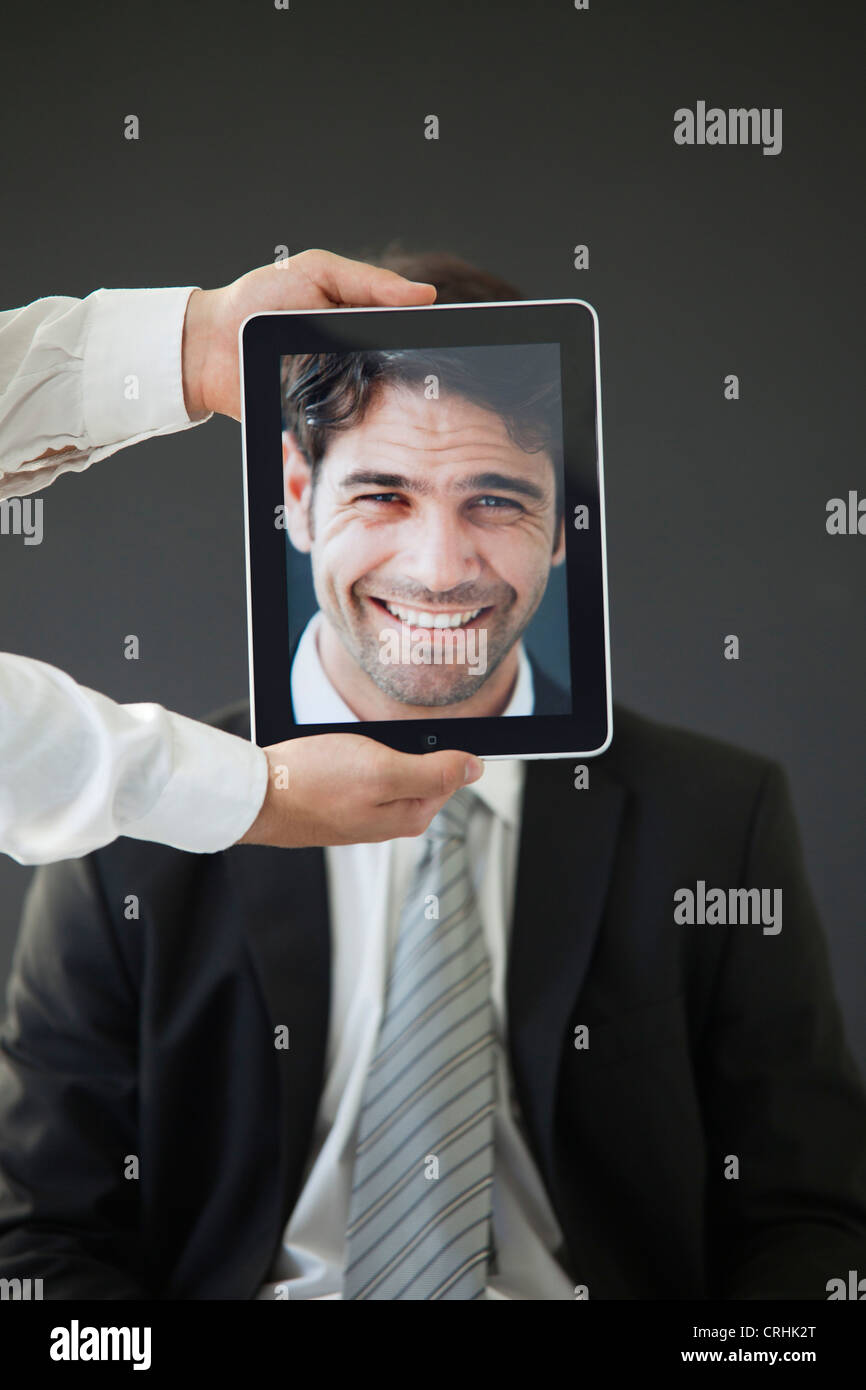 Man concealed behind digital tablet displaying image of smiling man Stock Photo