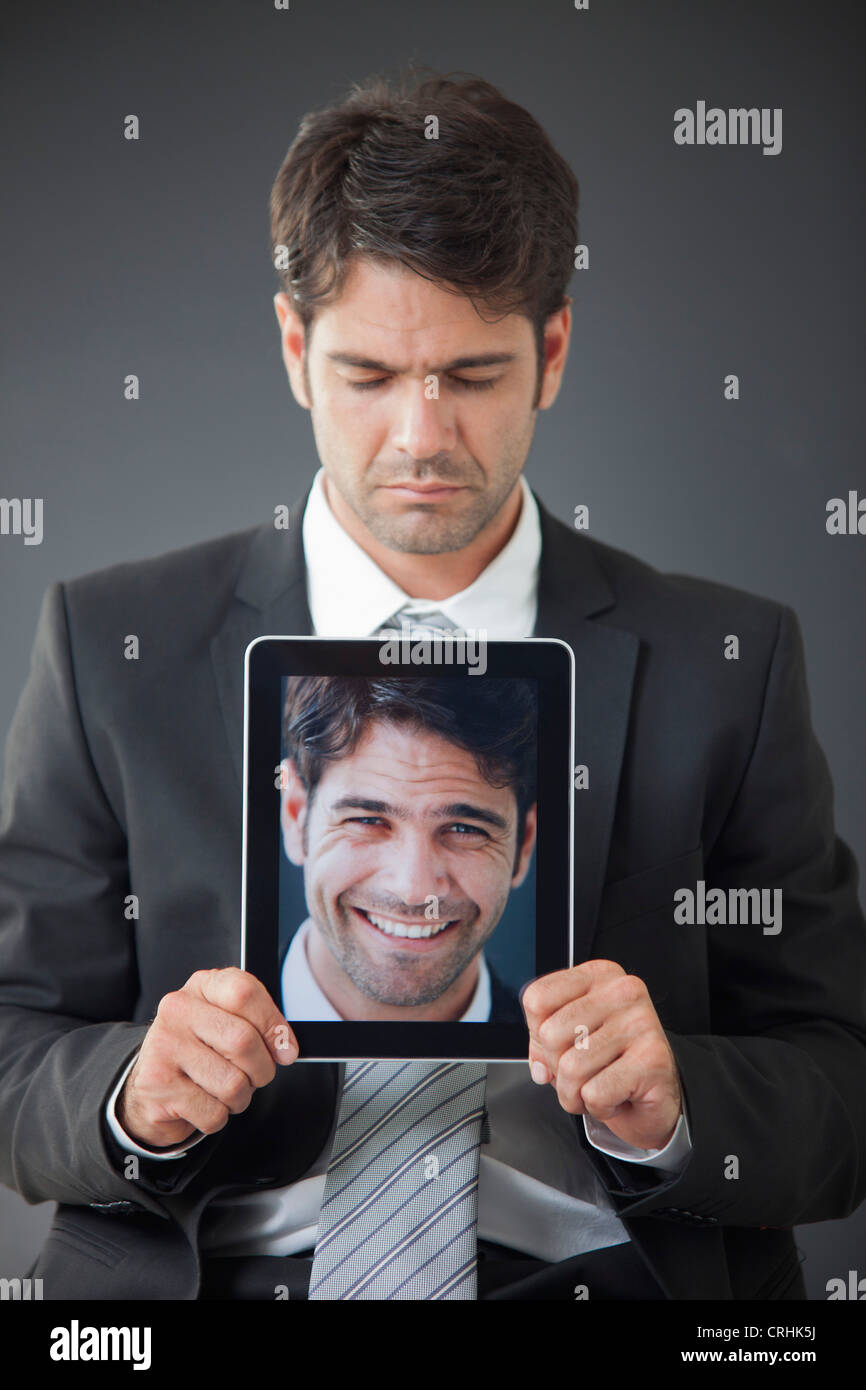 Man holding up digital tablet displaying image of himself smiling Stock Photo