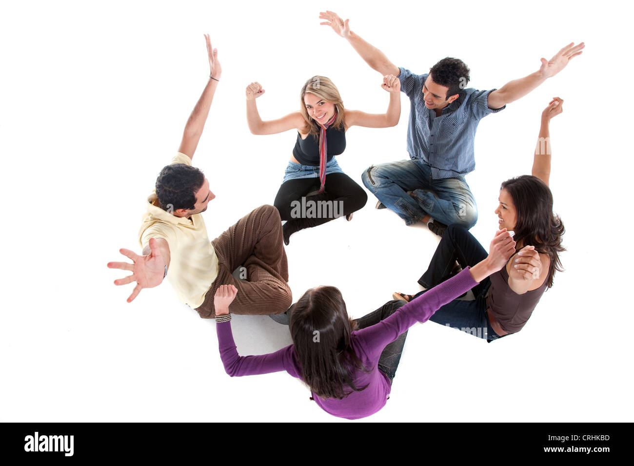 group of casual young people sitting in a circle on the floor, cheering with outstretched arms Stock Photo