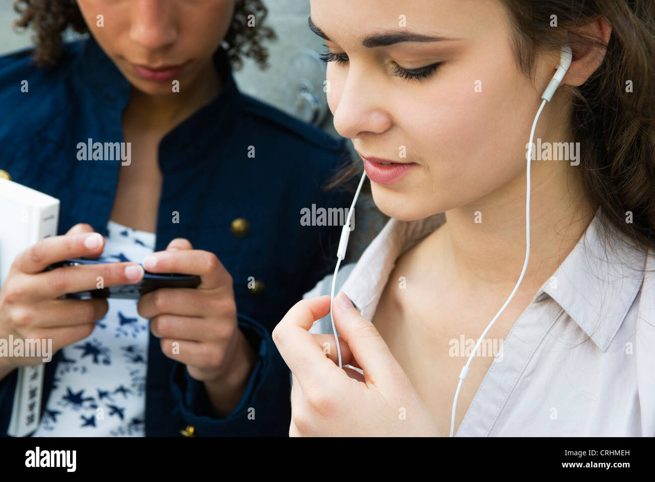 Young woman standing with friend, listening to earphones Stock Photo
