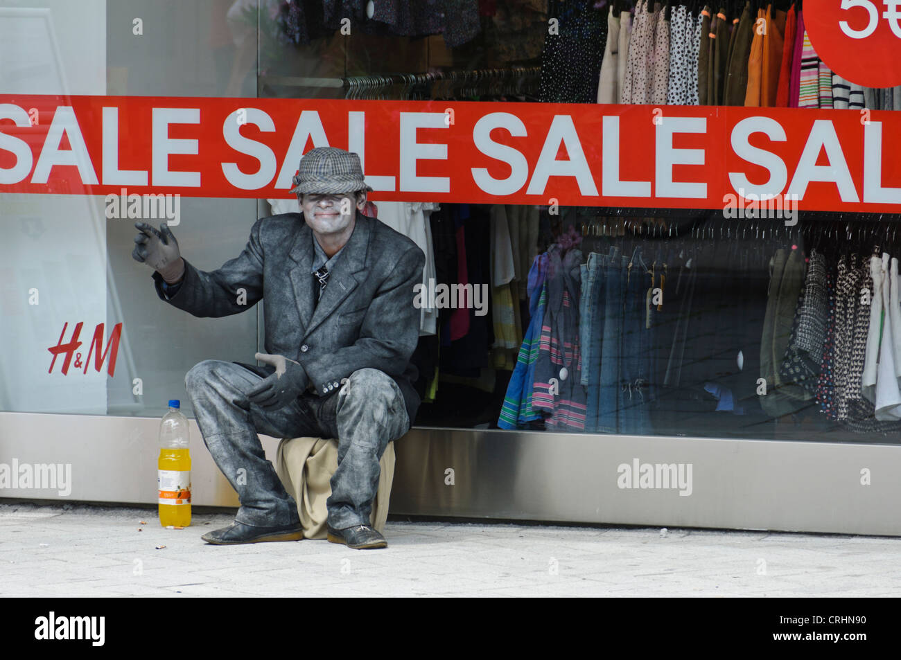 Mime Street Artist sitting in front a H&M Fashion Store Shop Window with 