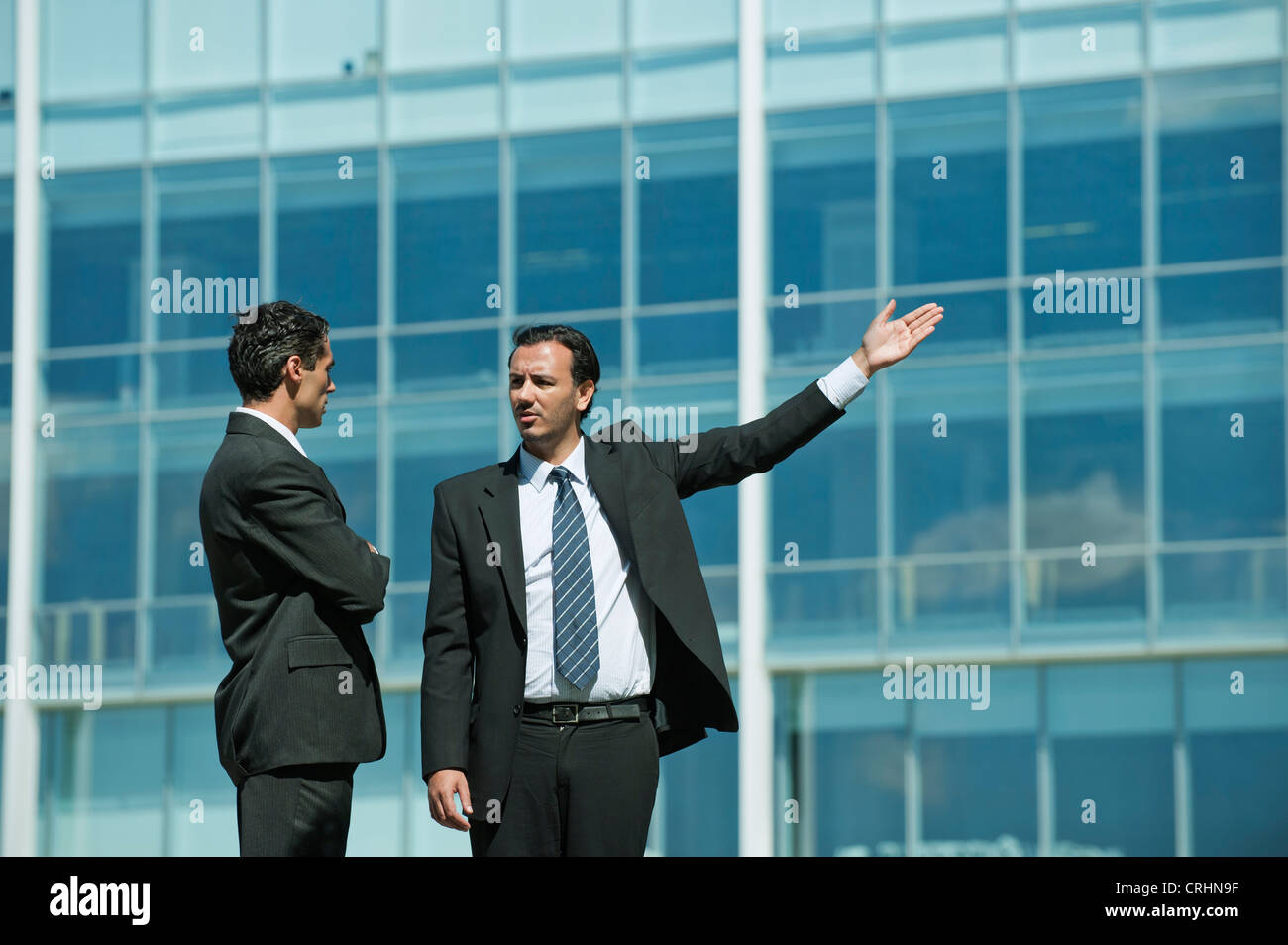 Business executives standing in front of office building, one pointing ...