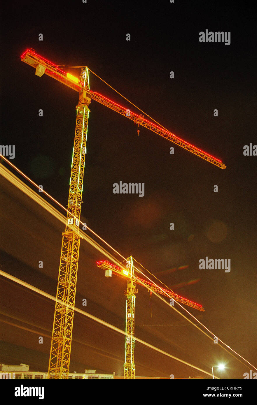 Construction cranes at night illuminated with light strip of traffic