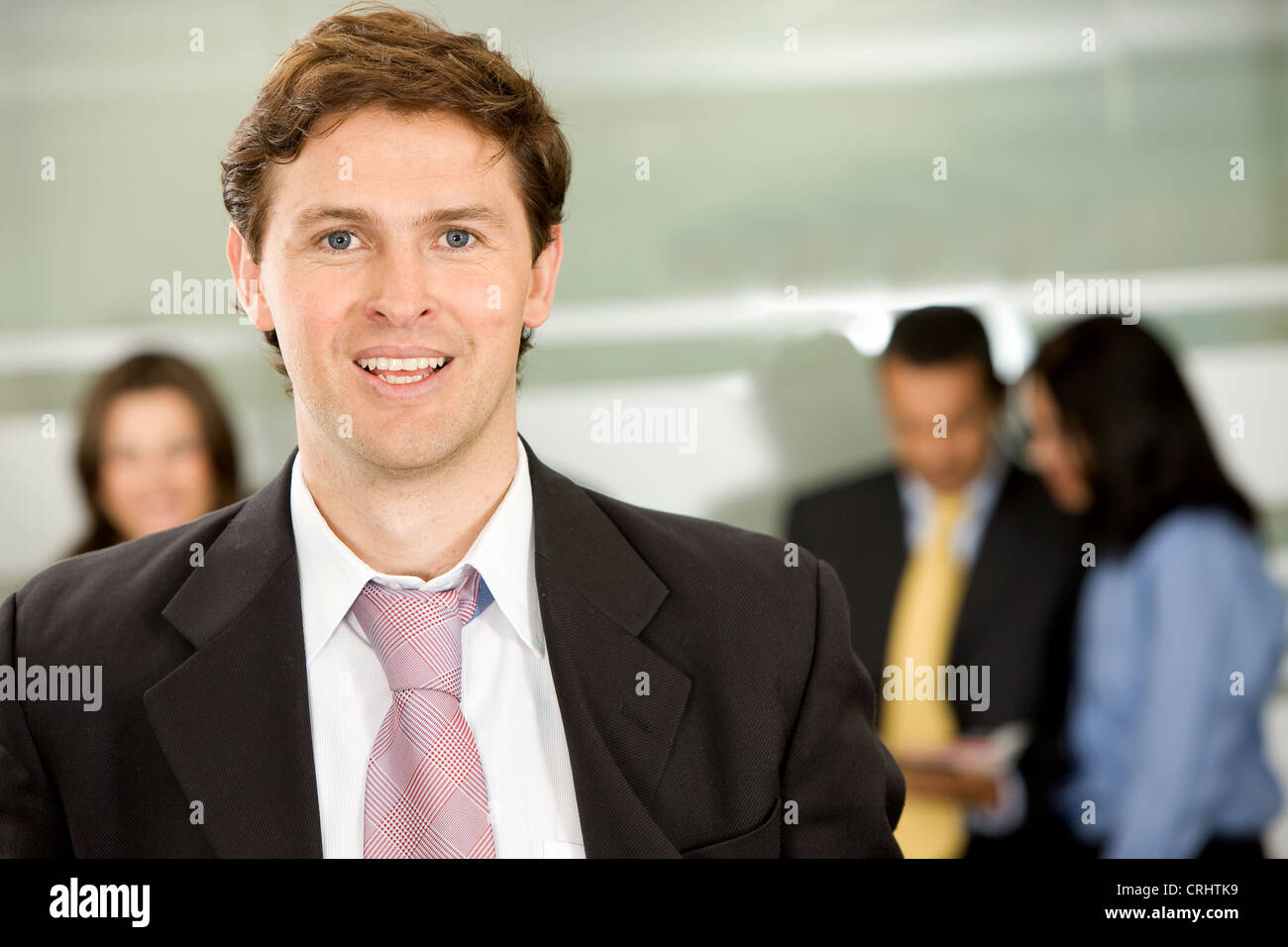 Businessman smiling in an office with his team behind him Stock Photo ...