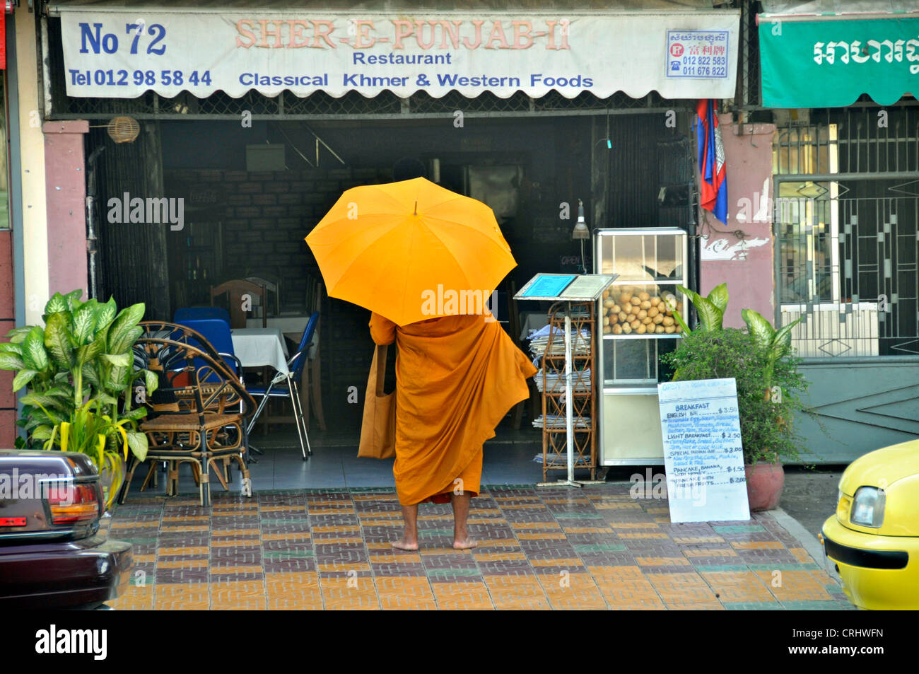 Buddhistic munk standing begging in front of a restaurant (Binhabad), Cambodia, Phnom Penh Stock Photo