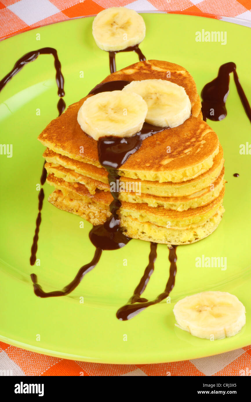 Heart shaped pancakes with chocolate sauce and banana slices on a green dish and a glass of milk beside. For Valentine's Day. Stock Photo