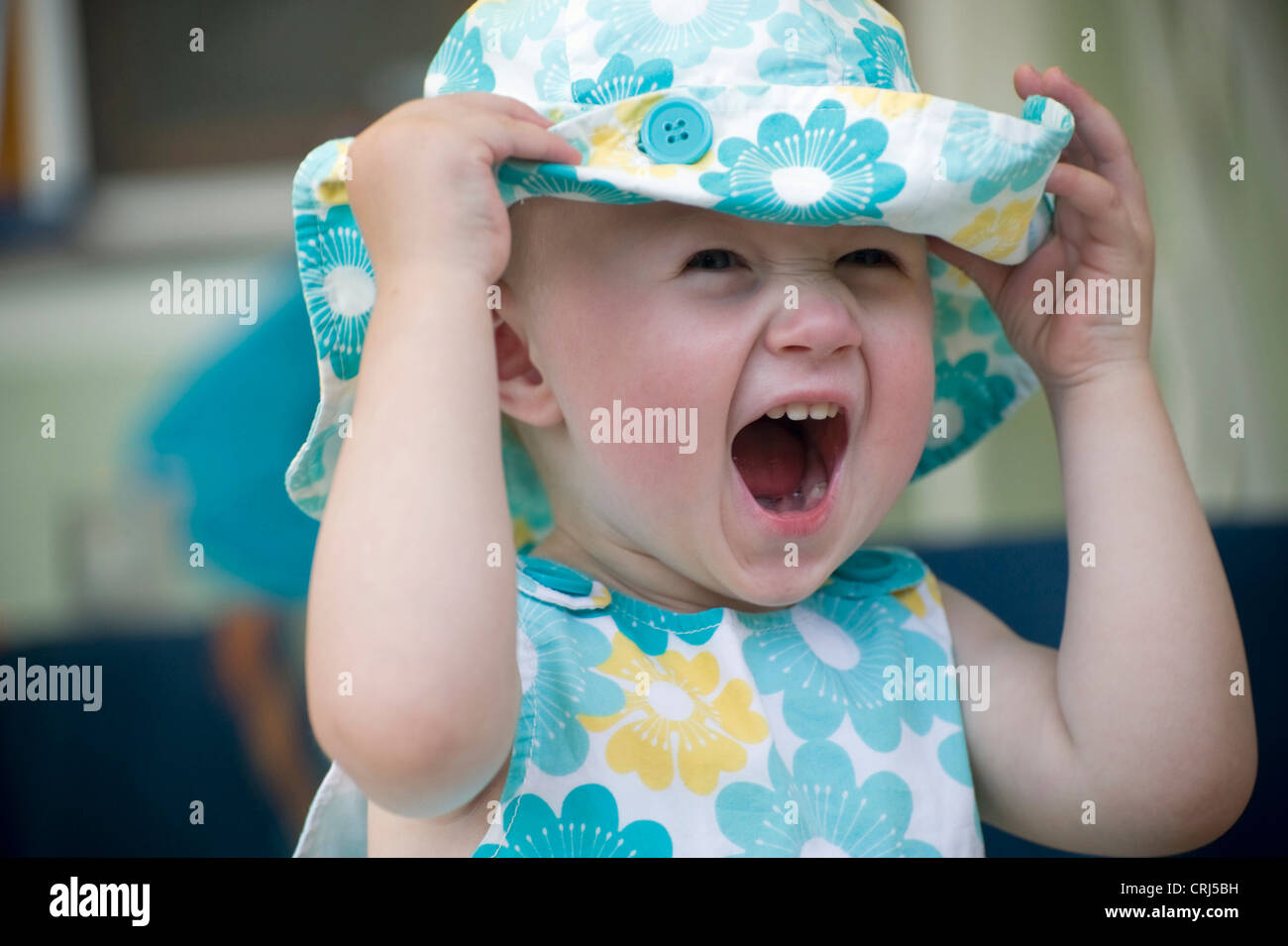baby in summer cloth holding her sunhead tight screaming jauntily Stock Photo