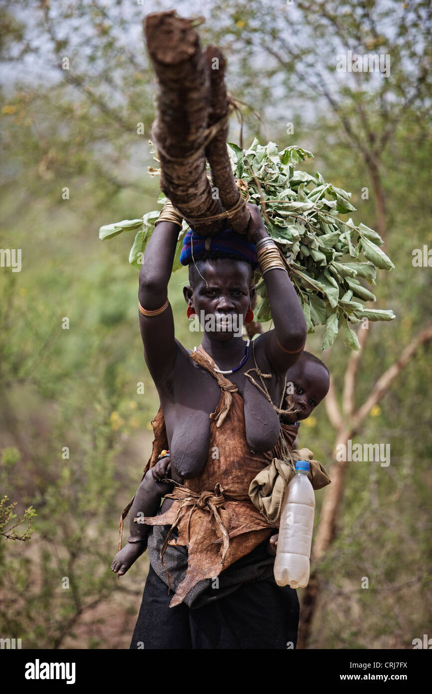 Tribal Bodi woman carrying a large piece of wood with her baby on the back. Stock Photo