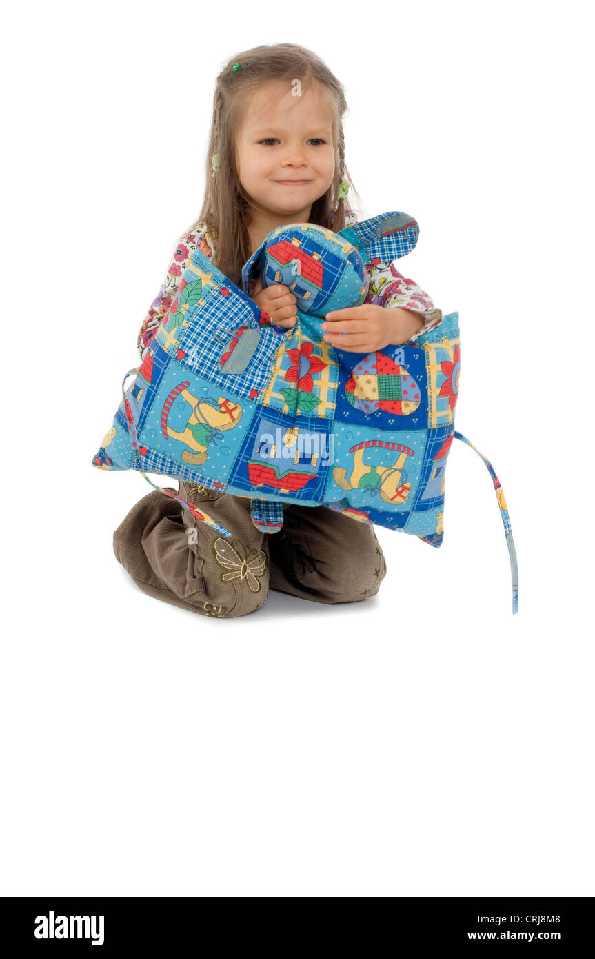 little girl happily kneeing on the floor holding a colourful seat cushion in front of her Stock Photo