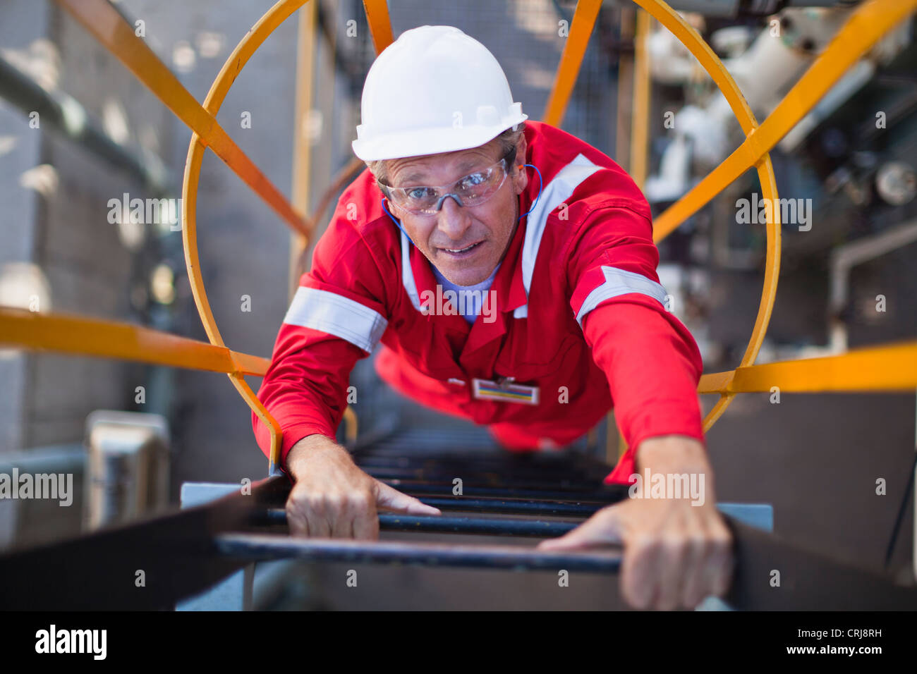 Worker climbing ladder at oil refinery Stock Photo