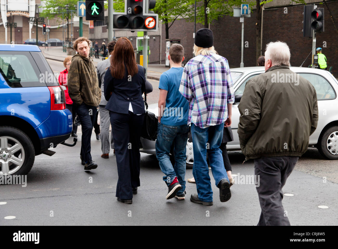 Traffic stopped across a pedestrian crossing on a road while the green man light shows, causing people to walk between cars. Nottingham, England, UK Stock Photo