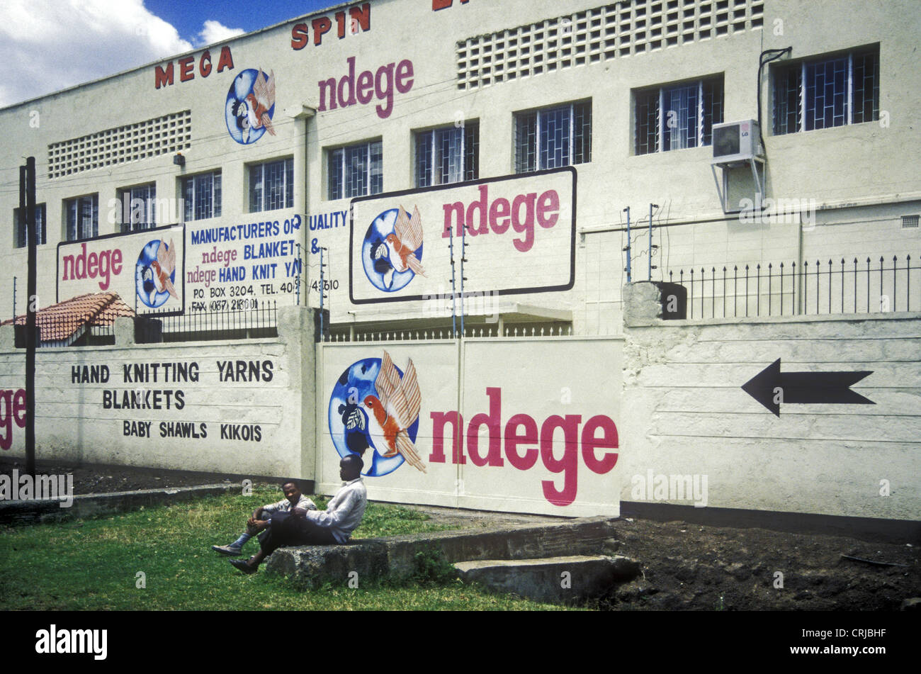 Ndege Blanket Factory Nakuru Kenya with sign writing advertisements with two men on grass verge Stock Photo