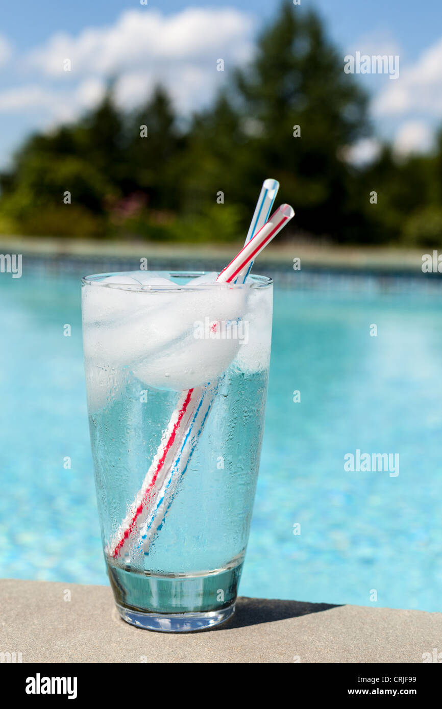 Glass of water with ice cubes at the side of a swimming pool Stock Photo
