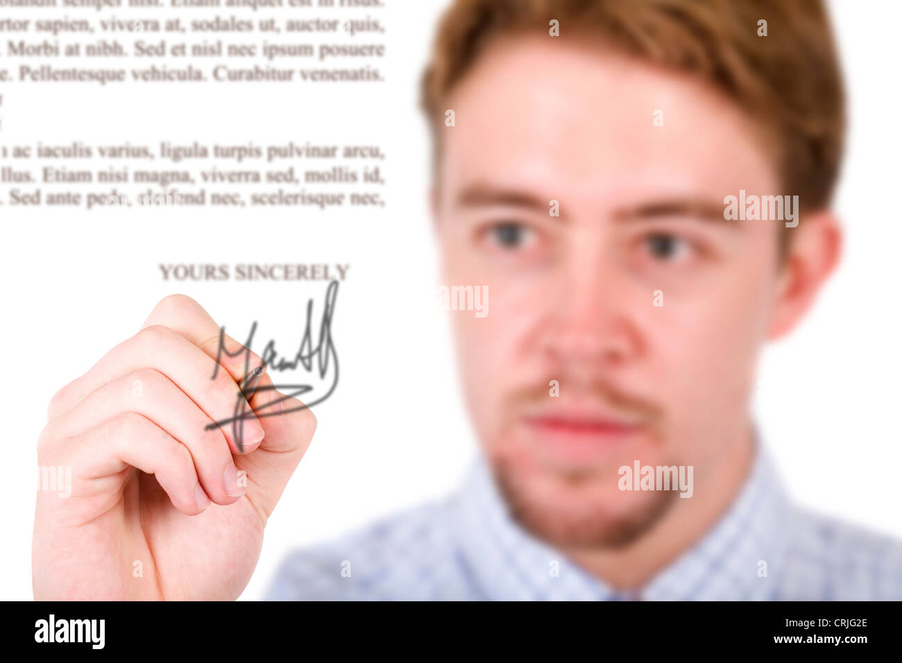 light brown young man with goatie signing a document projected on the screen in front of him Stock Photo