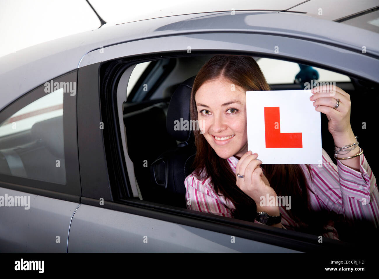 young woman sitting in a car holding up a sign with an 'L' (for 'learner'), United Kingdom Stock Photo