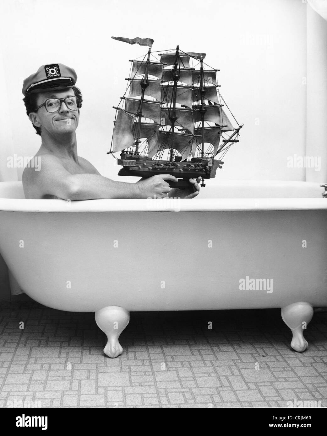 Man in captain hat holding toy ship in bathtub Stock Photo