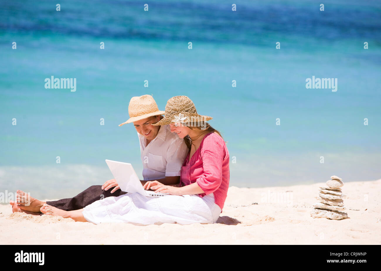 Happy couple using laptop on the beach, Maldives Stock Photo