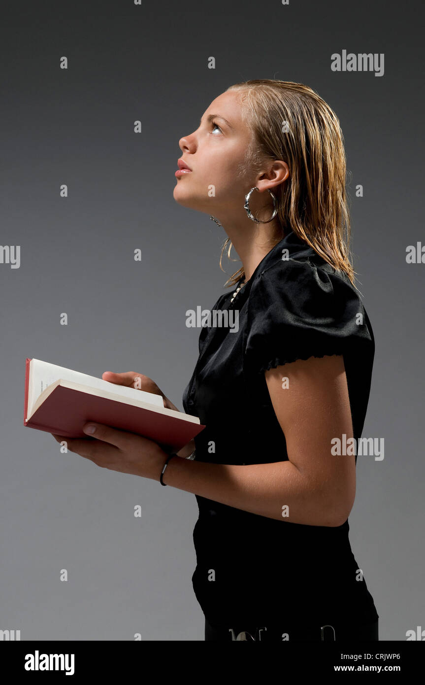 stylish blond young girl standing with a book in hands looking up lost in thought Stock Photo