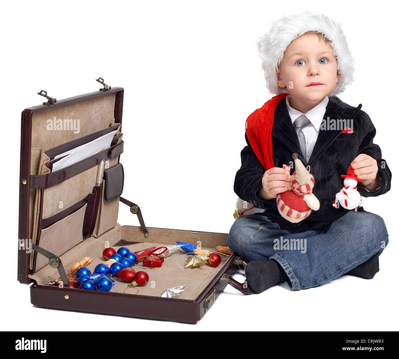 young boy with Santa cap sitting in front of a suitcase with Christmas accessories Stock Photo