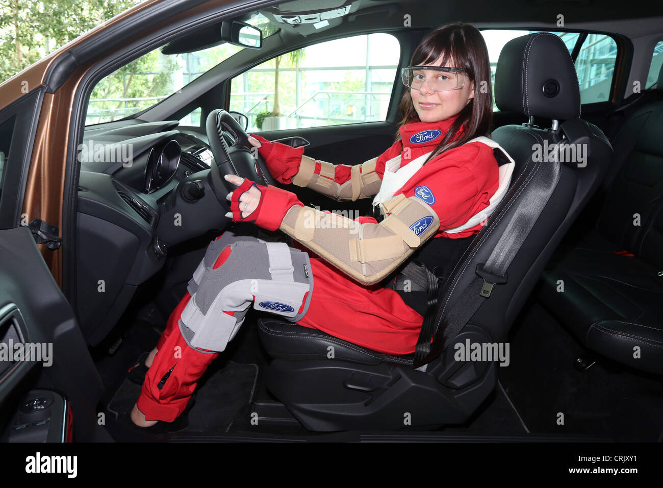 Woman dressed with an aging suit sits in a car. The suit (third age suit) gives the wearer the physical experience of being old. Stock Photo