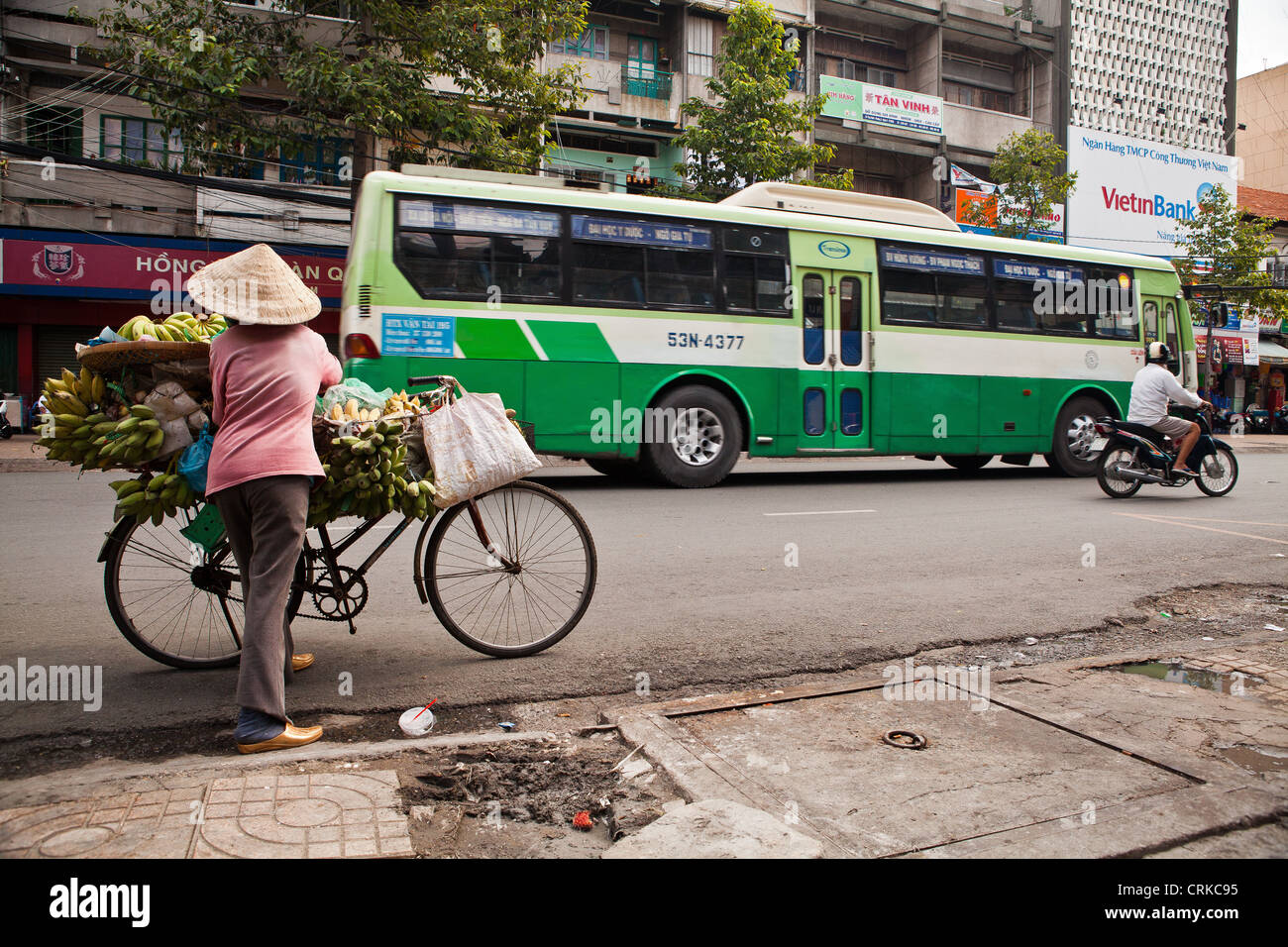 Life scene in the streets of HCMC : a lady making sure that her bike is stable enough before answering an approaching customer, Stock Photo